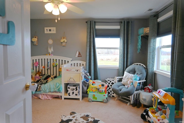 bedroom with carpet flooring, ceiling fan, a nursery area, and multiple windows