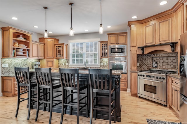 kitchen featuring dark stone countertops, light hardwood / wood-style flooring, pendant lighting, and appliances with stainless steel finishes