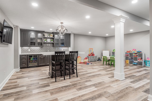 bar featuring decorative backsplash, light wood-type flooring, ornate columns, beverage cooler, and pendant lighting