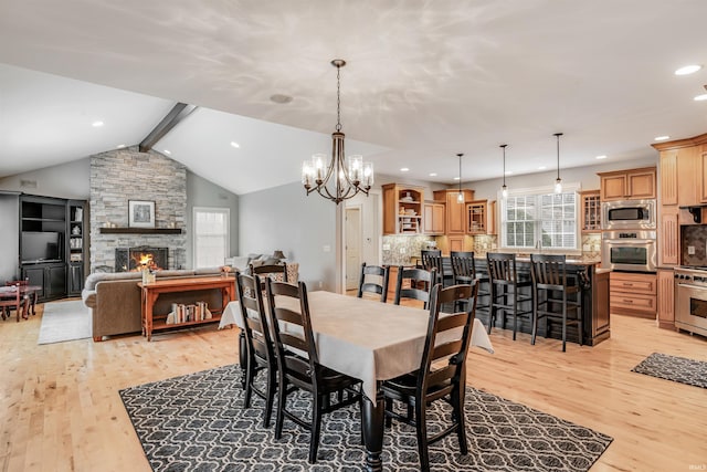 dining area featuring vaulted ceiling with beams, an inviting chandelier, a fireplace, and light hardwood / wood-style flooring