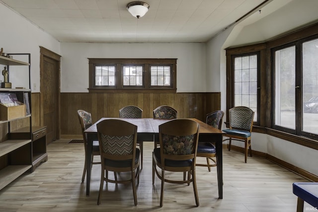 dining space with light hardwood / wood-style flooring, a healthy amount of sunlight, and wood walls