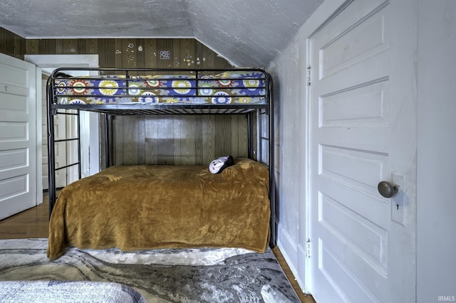 unfurnished bedroom with a textured ceiling, wood walls, wood-type flooring, and lofted ceiling