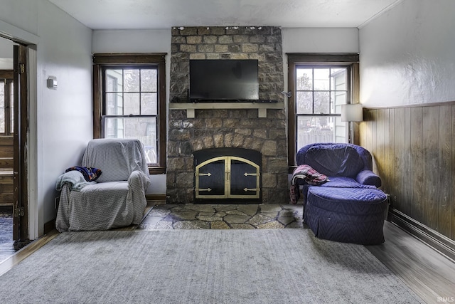 living room with hardwood / wood-style flooring, a healthy amount of sunlight, a stone fireplace, and wood walls