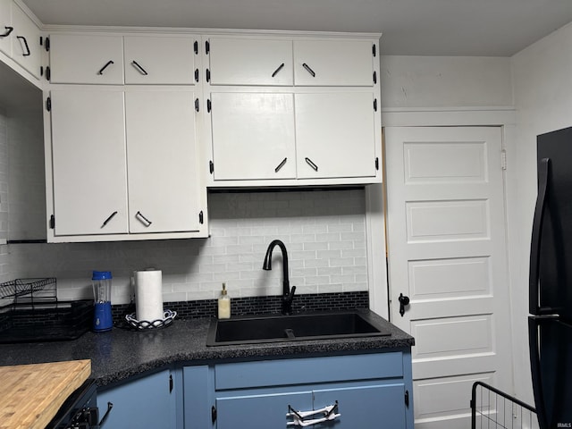 kitchen featuring white cabinets, backsplash, black refrigerator, and sink