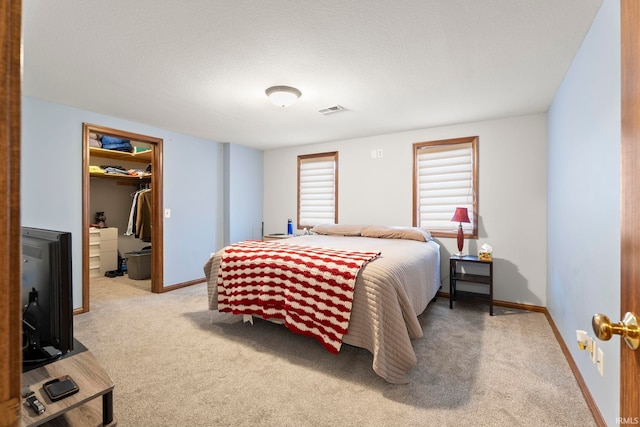 bedroom with a walk in closet, a closet, light colored carpet, and a textured ceiling