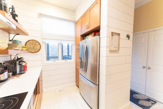 kitchen with wooden walls, light brown cabinetry, and stainless steel refrigerator with ice dispenser