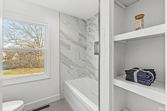 bathroom with tile patterned flooring, tiled shower / bath, and toilet