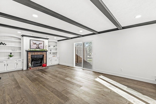 unfurnished living room with a brick fireplace, built in features, a textured ceiling, beamed ceiling, and wood-type flooring