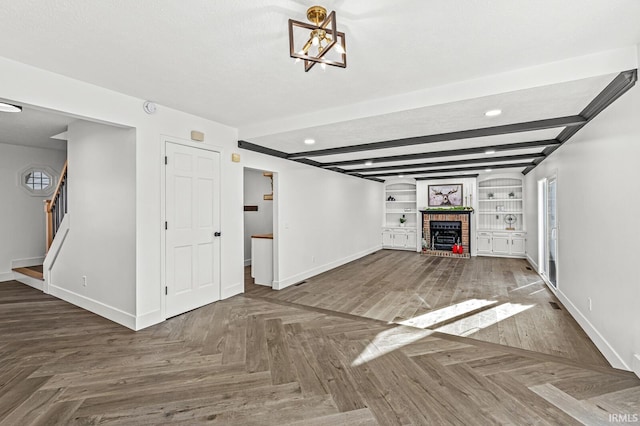 unfurnished living room with built in shelves, a textured ceiling, a brick fireplace, and beam ceiling