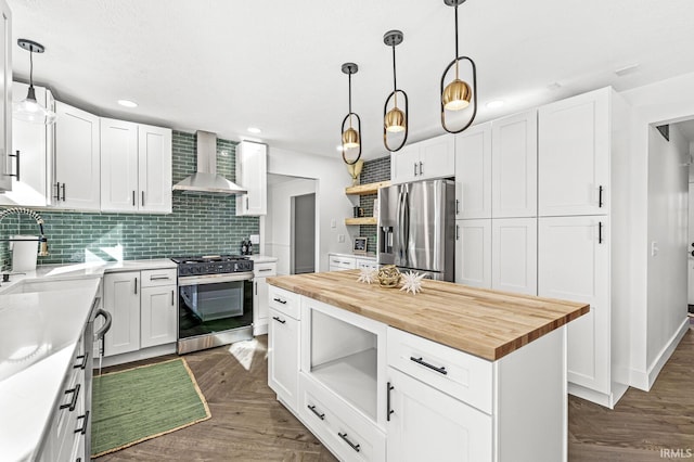 kitchen with stainless steel appliances, wall chimney range hood, wooden counters, pendant lighting, and white cabinets