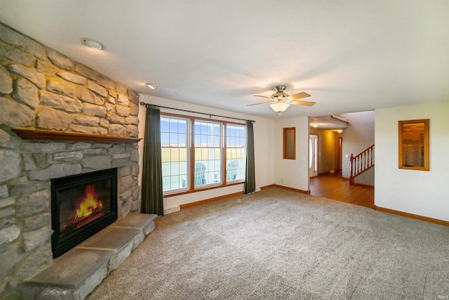 unfurnished living room with carpet, a stone fireplace, and ceiling fan