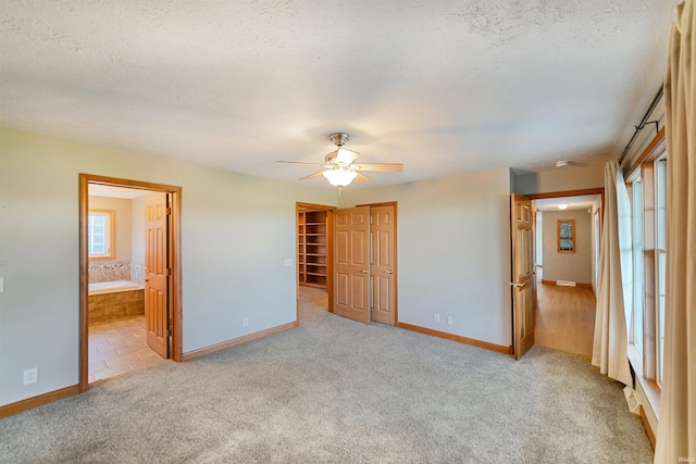 unfurnished bedroom featuring ceiling fan, light colored carpet, ensuite bathroom, and a closet