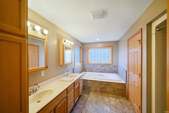 bathroom featuring a relaxing tiled tub, a textured ceiling, and vanity