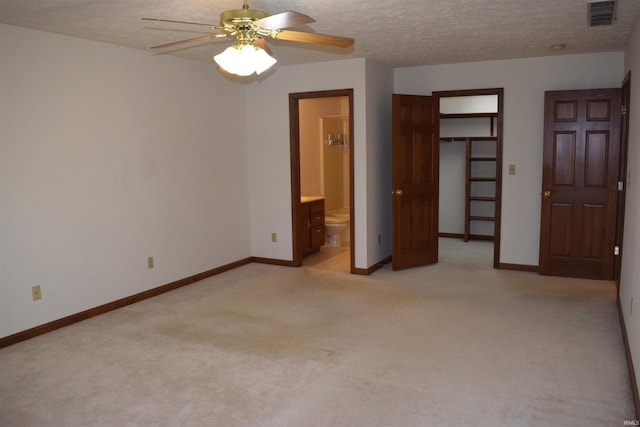 unfurnished bedroom with a textured ceiling, ensuite bathroom, ceiling fan, and light carpet