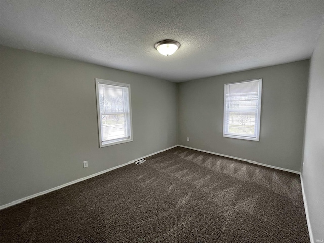 unfurnished room featuring a wealth of natural light, a textured ceiling, and dark colored carpet