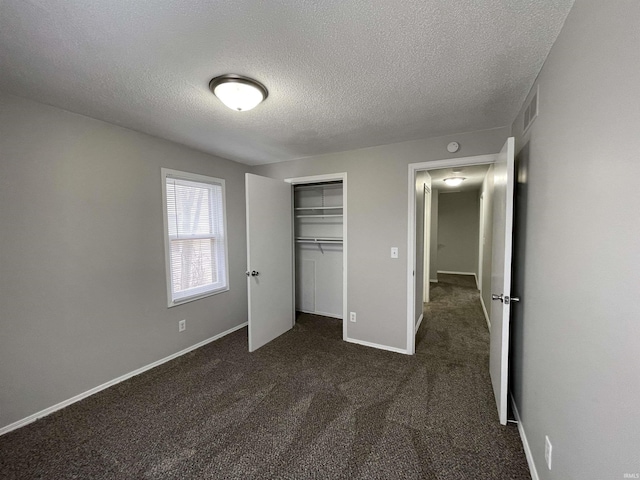 unfurnished bedroom featuring dark carpet, a textured ceiling, and a closet