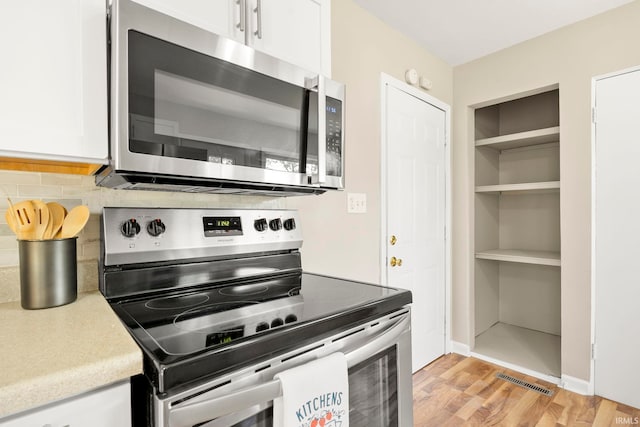 kitchen with white cabinets, light wood-type flooring, stainless steel appliances, and backsplash