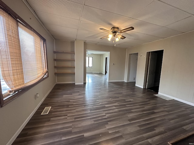 empty room featuring built in shelves, a wealth of natural light, ceiling fan, and dark wood-type flooring