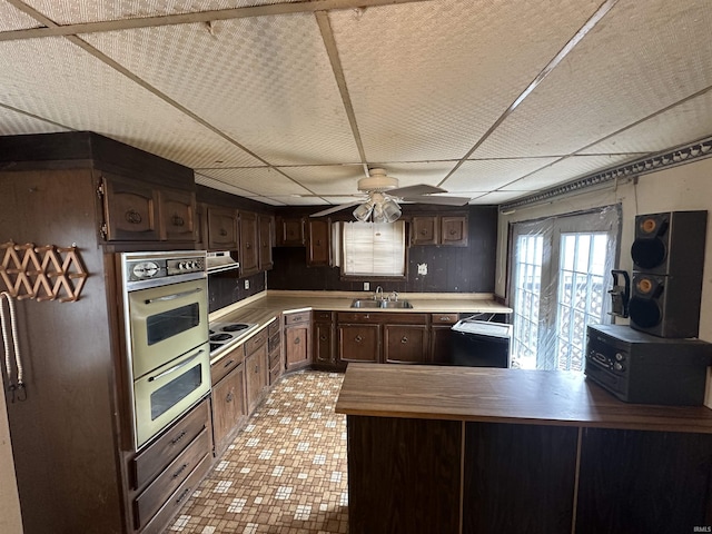 kitchen with kitchen peninsula, dark brown cabinetry, double oven, sink, and white electric cooktop