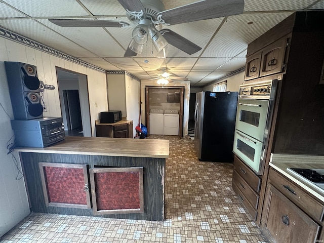 kitchen featuring appliances with stainless steel finishes, dark brown cabinets, washer and clothes dryer, and wood walls