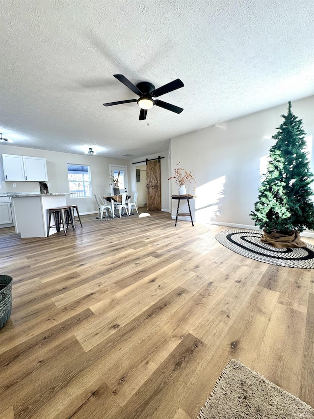 unfurnished room with a textured ceiling, a barn door, light hardwood / wood-style flooring, and ceiling fan