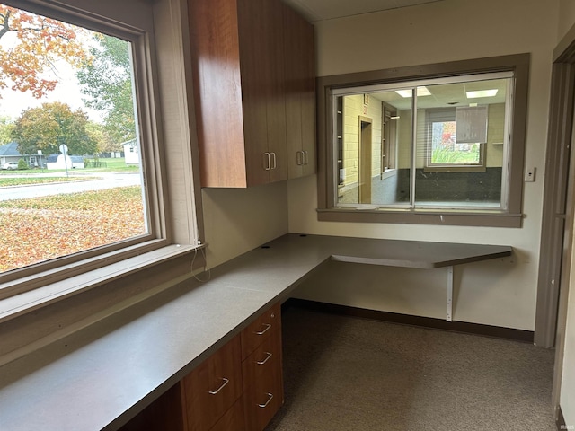 unfurnished office featuring built in desk, a healthy amount of sunlight, and dark carpet