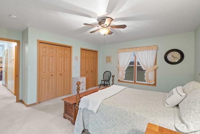 bedroom with ceiling fan, light colored carpet, and two closets