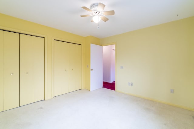 unfurnished bedroom with ceiling fan, light colored carpet, and multiple closets