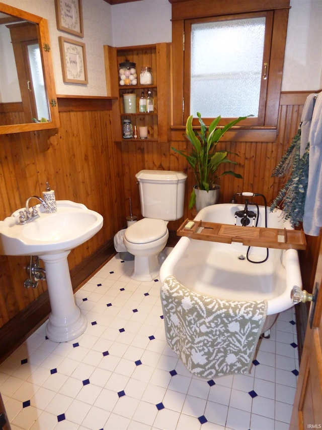 bathroom with tile patterned flooring, wood walls, toilet, and a tub to relax in