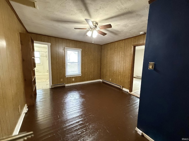 empty room with a textured ceiling, dark wood-type flooring, wooden walls, and a baseboard radiator