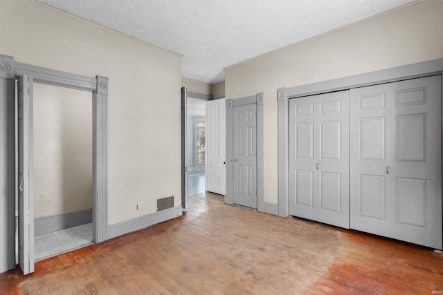 unfurnished bedroom featuring two closets, a textured ceiling, and light hardwood / wood-style floors