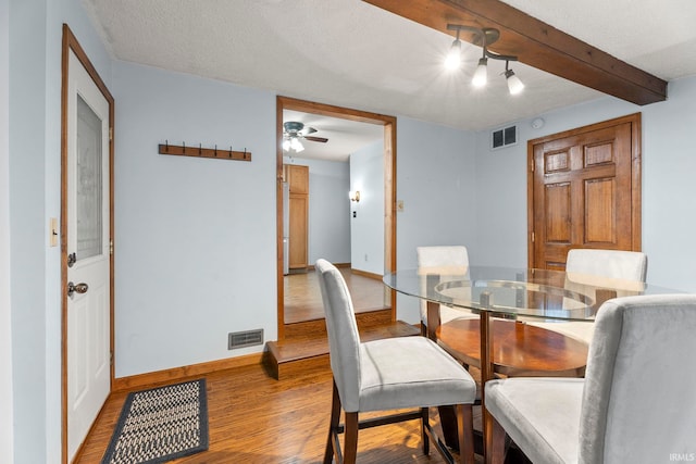 dining room featuring ceiling fan, beam ceiling, wood-type flooring, and a textured ceiling