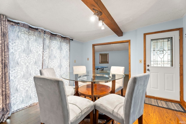 dining area with hardwood / wood-style flooring, vaulted ceiling with beams, and a textured ceiling