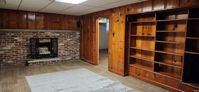 unfurnished living room featuring a fireplace, wood walls, light hardwood / wood-style flooring, and a drop ceiling