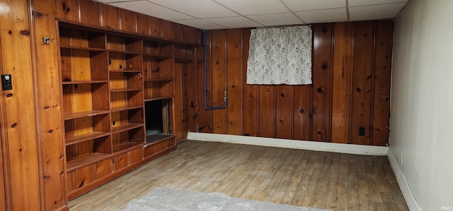 living room with a paneled ceiling, light hardwood / wood-style floors, and wood walls