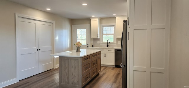 kitchen with dishwasher, sink, a kitchen island, hardwood / wood-style floors, and white cabinets