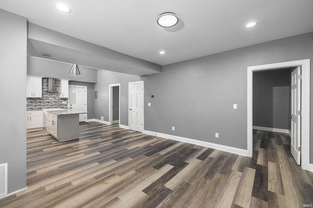 kitchen featuring wall chimney range hood, pendant lighting, a center island, dark hardwood / wood-style floors, and white cabinetry