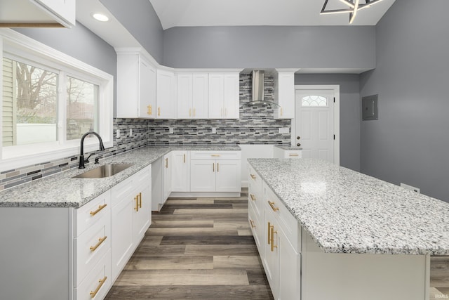 kitchen with dark hardwood / wood-style flooring, wall chimney range hood, sink, a center island, and white cabinetry