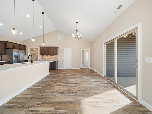 kitchen with lofted ceiling, stainless steel fridge, dark brown cabinetry, and hanging light fixtures