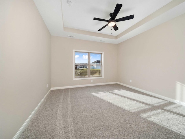 empty room with ceiling fan, carpet floors, and a tray ceiling