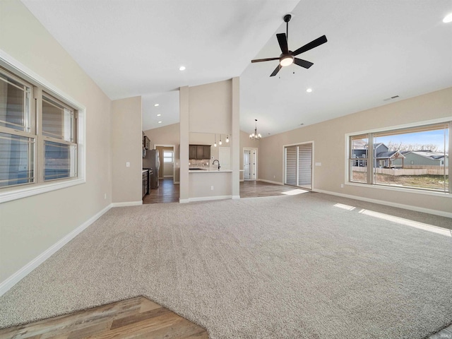 unfurnished living room featuring sink, high vaulted ceiling, wood-type flooring, and ceiling fan with notable chandelier