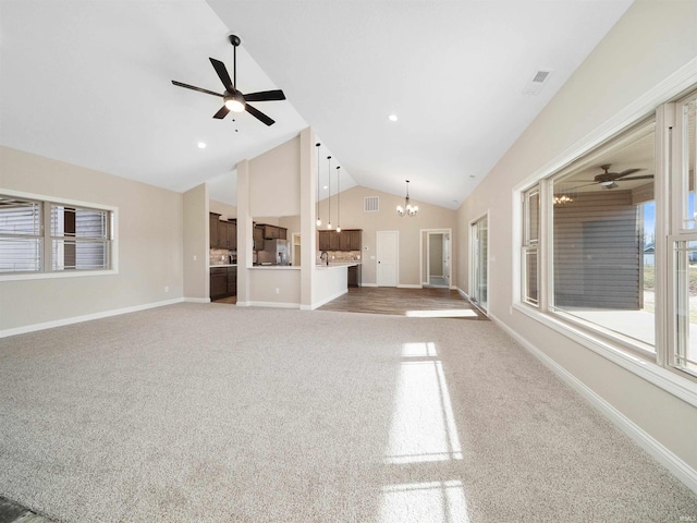 unfurnished living room featuring ceiling fan with notable chandelier, carpet floors, and vaulted ceiling