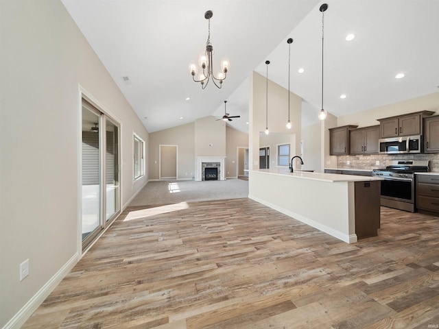 kitchen with pendant lighting, light hardwood / wood-style floors, a kitchen island with sink, dark brown cabinets, and appliances with stainless steel finishes