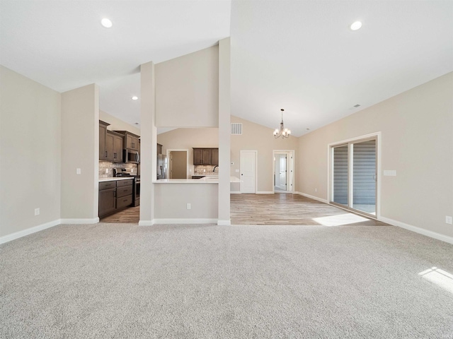 unfurnished living room with a chandelier, light carpet, and vaulted ceiling