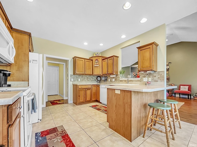 kitchen featuring kitchen peninsula, decorative backsplash, white appliances, and a breakfast bar