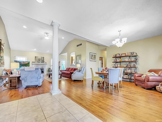 living room featuring ceiling fan with notable chandelier, lofted ceiling, a fireplace, and light hardwood / wood-style flooring