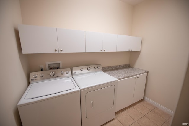 clothes washing area featuring cabinets, light tile patterned floors, and washing machine and clothes dryer