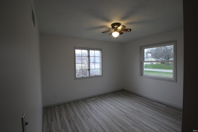 unfurnished room with a textured ceiling, light wood-type flooring, and ceiling fan