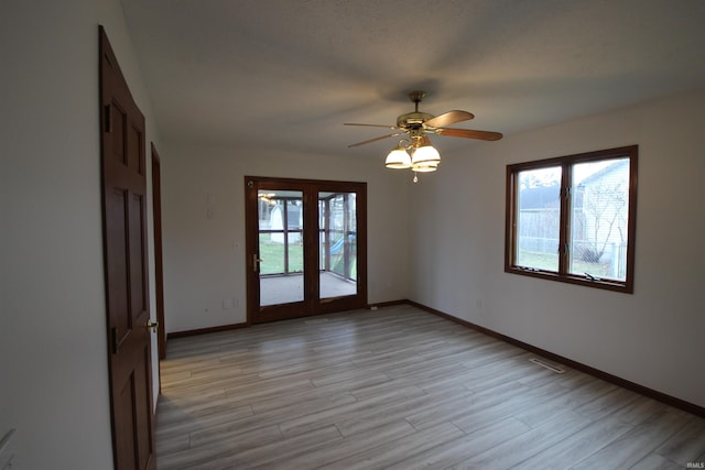 empty room with ceiling fan, light hardwood / wood-style flooring, a healthy amount of sunlight, and french doors