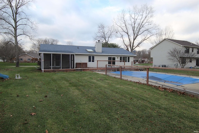 back of property with a sunroom, a covered pool, a lawn, and a chimney